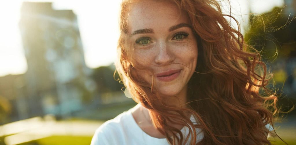 Portraits of a charming red-haired girl with a cute face. Girl posing for the camera in the city center. She has a wonderful mood and a lovely smile.